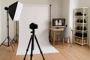 Modern home photography studio setup with softbox lights, backdrop stands, tripod, computer desk, and organized storage shelves
